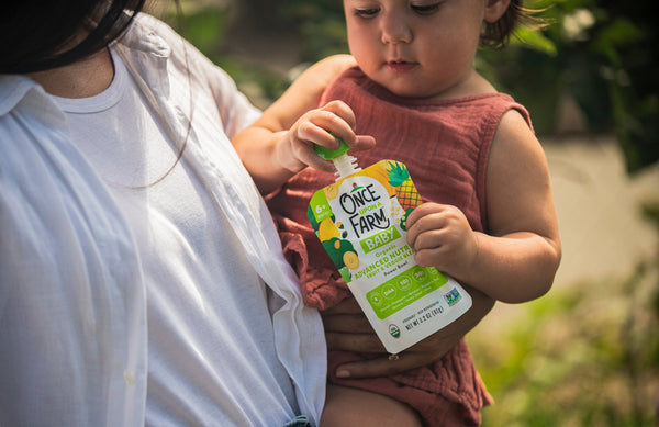 mom holding baby, who is holding a Once Upon a Farm Advanced Nutrition blend pouch