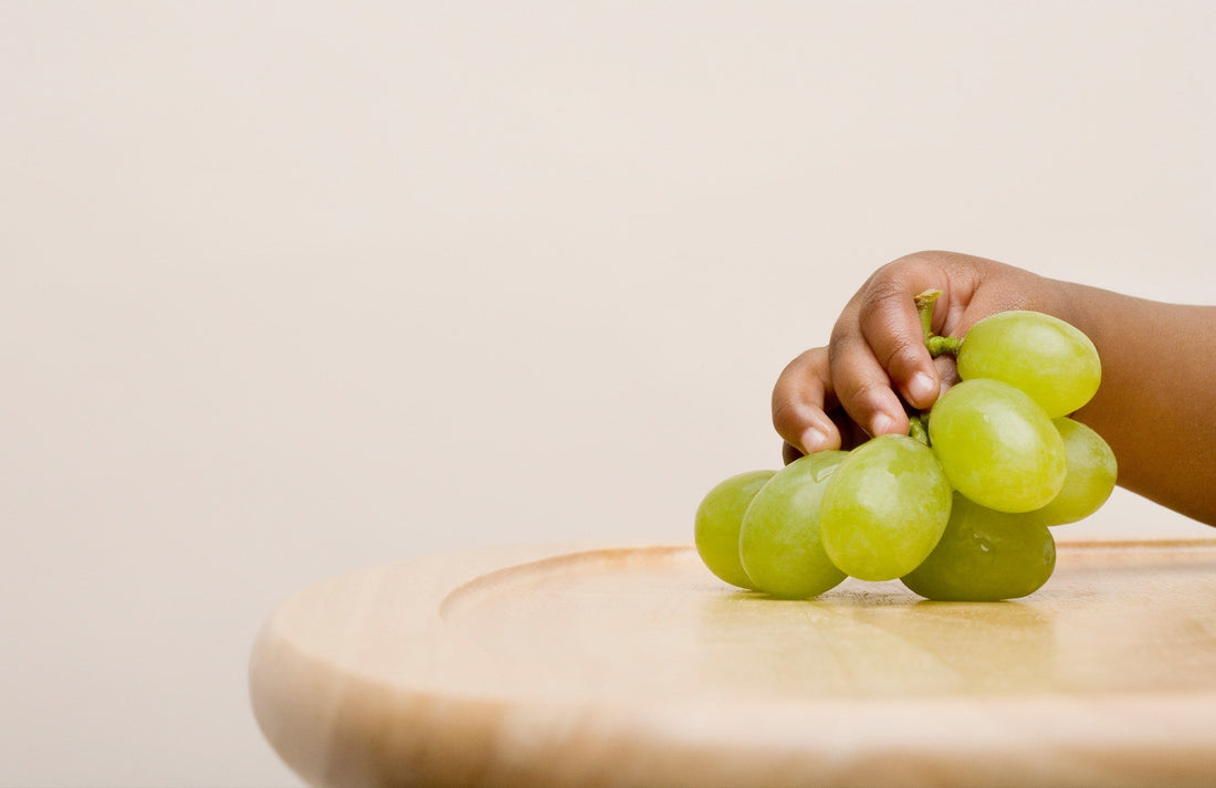 toddler's hand reaching for grapes on a tray