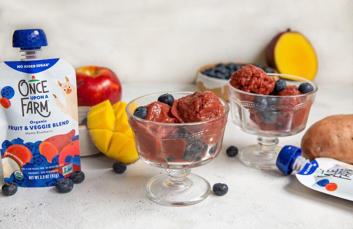 blueberry mango sorbet in dessert cups, with fresh mango and a Once Upon a Farm pouch next to them