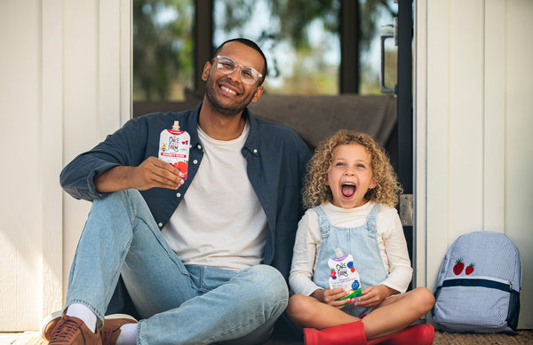 dad and daughter, smiling while each holding a once upon a farm pouch
