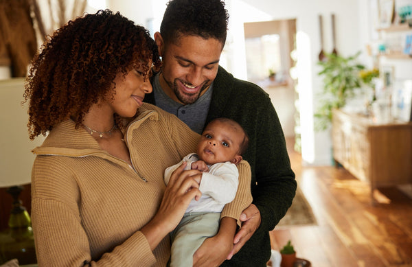 mom holding a newborn baby, while dad wraps his arms around the both of them