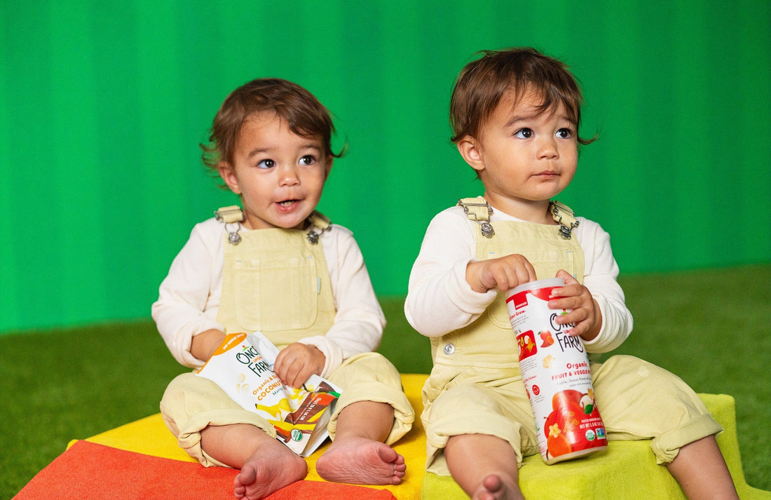 two toddlers, one holding a bag of coconut melts and the other holding a canister of puffs
