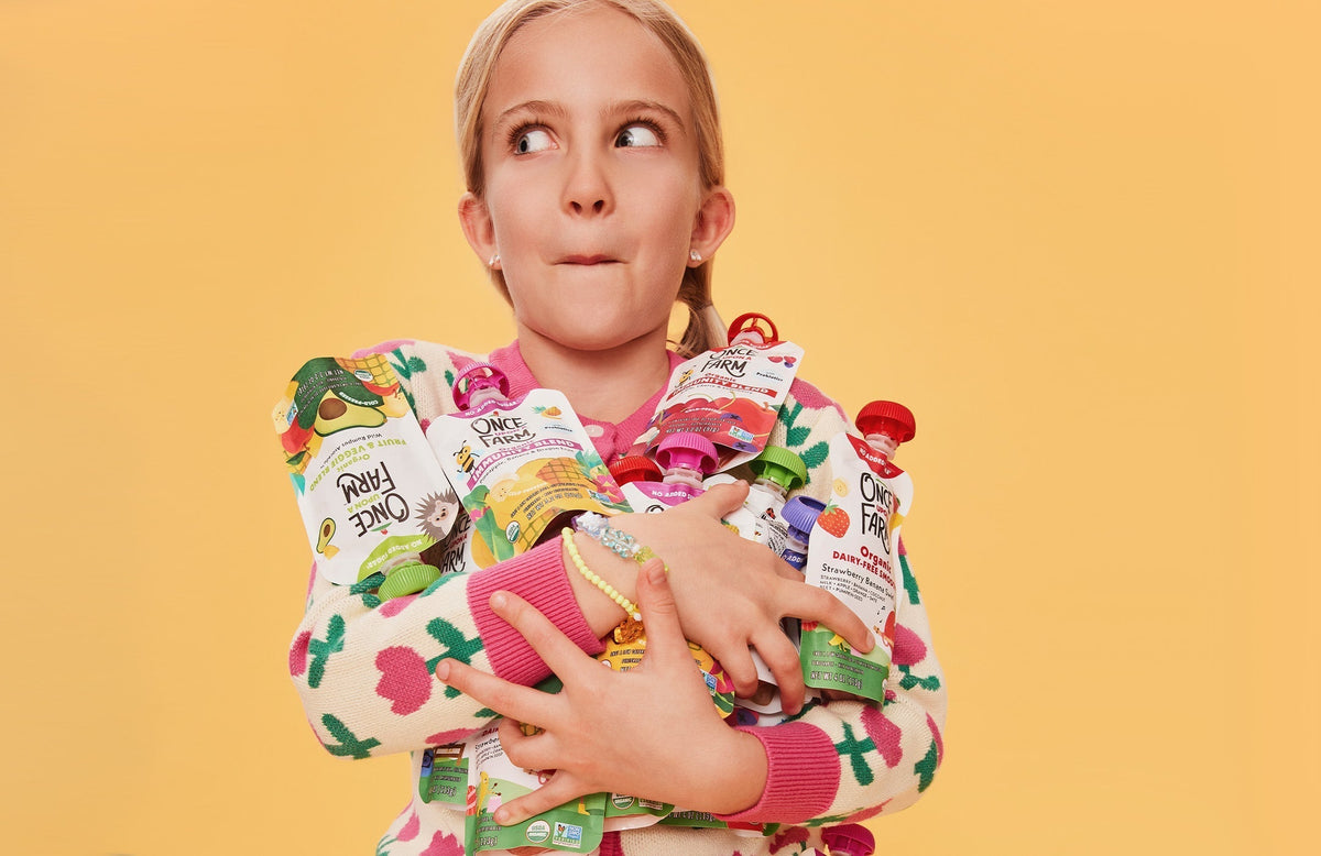 girl holding lots of Once Upon a Farm pouches in her arms