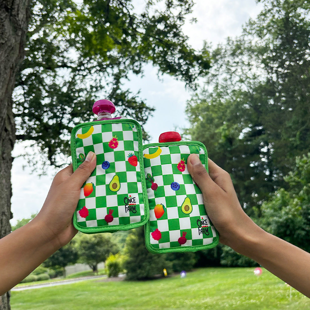 Two green checkered pouch coolers with fruit designs held up outdoors.