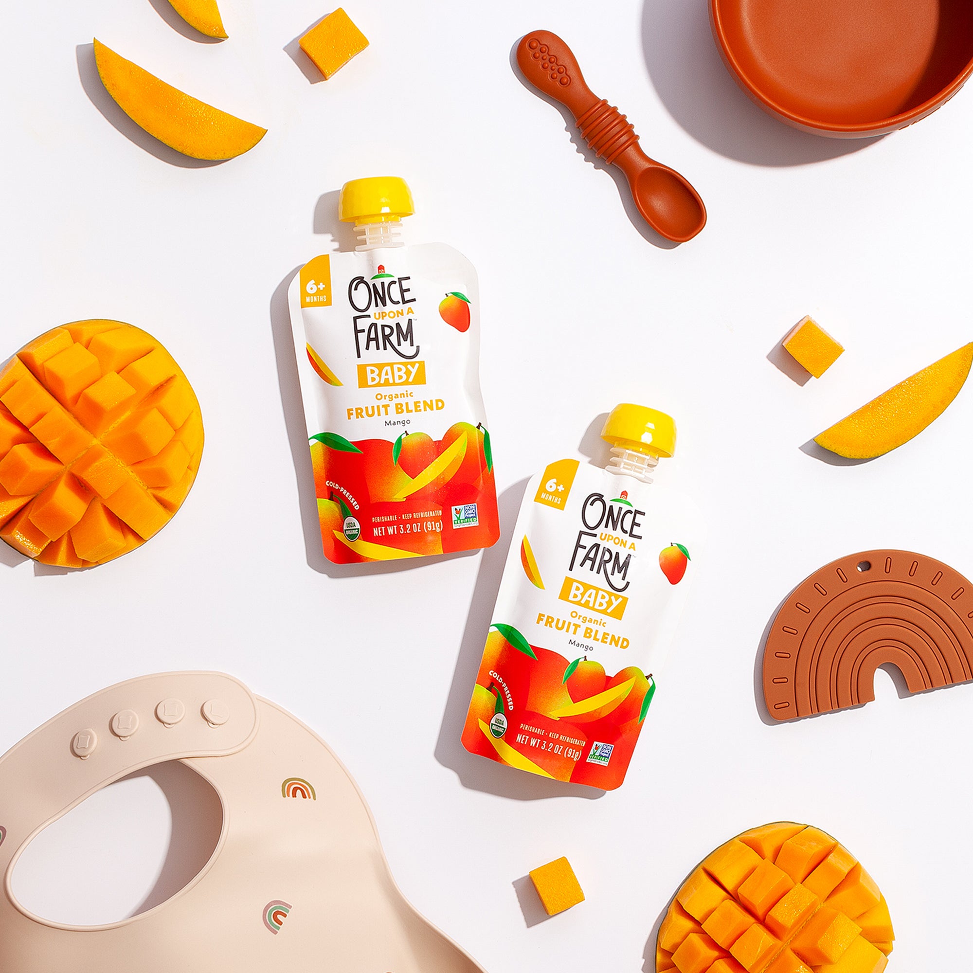 Photo of two Mango Baby Blends with mangoes, a bib, and bowl in the background.